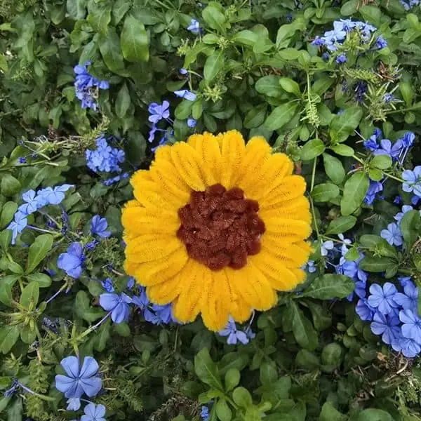Flor artesanal tipo girasol en amarillo vivo con centro marrón rojizo y textura aterciopelada